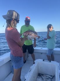 A group of anglers celebrating a successful catch of a Snapper while out on a fishing charter in open waters.