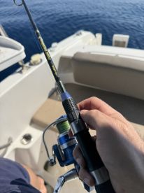 A close-up of a hand gripping a fishing rod and reel on a boat, showcasing the excitement of fishing in open waters.