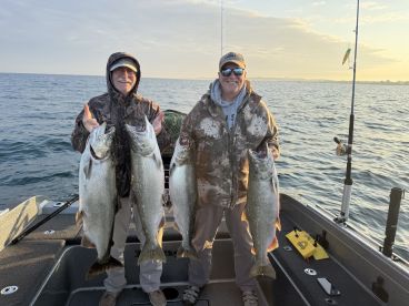 Two anglers proudly displaying their catch of large Lake Trout while fishing on a boat during a serene morning on the water.