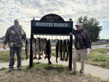 Two anglers proudly displaying their catch of multiple Salmon at Manistee Harbor, showcasing a successful fishing trip.
