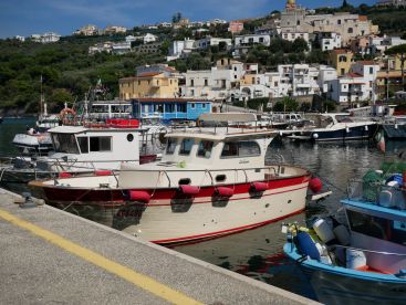 A scenic view of a fishing boat docked in a picturesque harbor, surrounded by colorful buildings and other vessels.