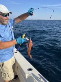 An angler reeling in a Redfish while fishing on a boat in clear waters, showcasing the excitement of the catch.