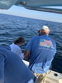 A young angler is engaged in reeling in a fish while fishing on a boat, showcasing an exciting moment on the water.
