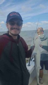 An angler proudly displaying a caught shark while fishing on a boat, with another fisherman in the background.