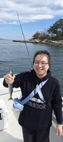 An angler proudly displaying a freshly caught mackerel while fishing on a boat in a scenic coastal environment.