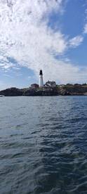 A scenic view of a lighthouse on a rocky shore, captured from a boat in open water, showcasing a beautiful coastal environment.