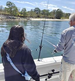 A young angler and an adult fishing together on a boat, casting lines in a serene coastal environment.