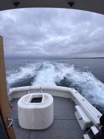 A scenic view from the back of a fishing boat, showcasing the wake and cloudy sky while heading out to sea.