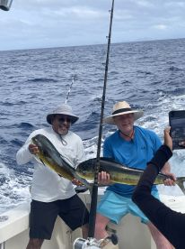 Two anglers proudly displaying their catch of Mahi Mahi while fishing offshore, showcasing a successful day on the water.