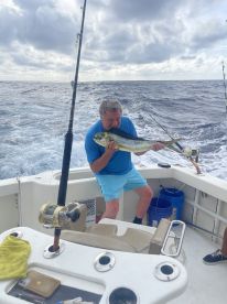 An angler proudly displaying a large Mahi Mahi while fishing on a charter boat in open waters.