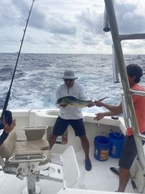 Anglers aboard a fishing boat actively reeling in a vibrant Mahi Mahi during a deep-sea fishing trip.
