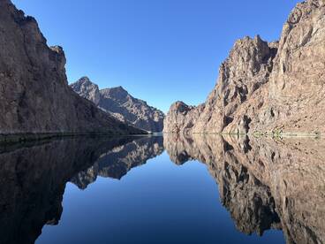 Scenic view of a calm waterway surrounded by rugged mountains, reflecting the clear blue sky.