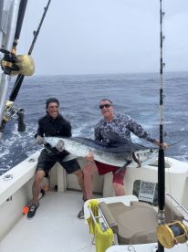 Two anglers celebrating a successful catch of a large Marlin aboard a sportfishing boat in rough seas.