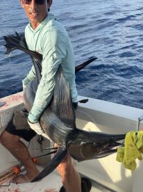 Angler proudly displaying a large Sailfish while aboard a sport fishing boat, showcasing the thrill of deep-sea fishing.