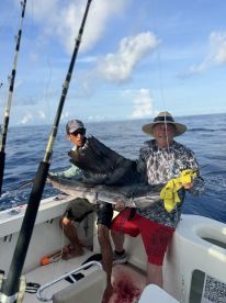 Two anglers proudly displaying a large Sailfish aboard a fishing boat in open waters.