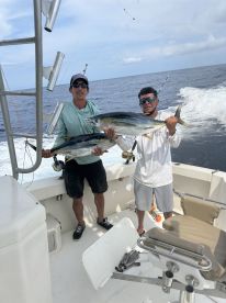 Two anglers proudly displaying their catch of Yellowfin Tuna aboard a sport fishing boat in open waters.