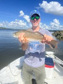 Angler proudly displaying a Redfish while fishing from a small boat under a bright blue sky.