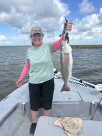 An angler proudly displaying a large Redfish while fishing from a boat in a coastal waterway.