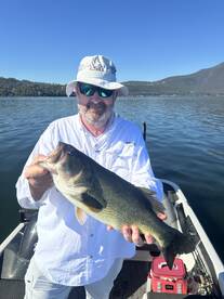 An angler proudly displaying a large Largemouth Bass while fishing on a serene lake, showcasing a beautiful day on the water.