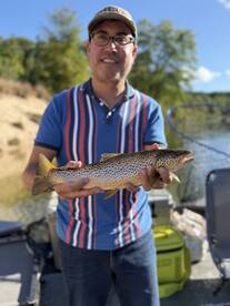 Angler proudly displaying a beautiful Brown Trout while fishing from a boat in a serene lake setting.