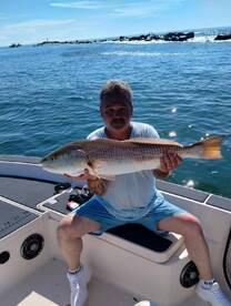 An angler proudly displaying a large Redfish while seated on a boat, enjoying a sunny day on the water.
