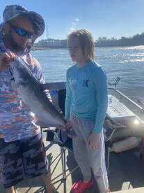 A young angler proudly displays a caught catfish while fishing on a sunny day, showcasing a family-friendly fishing experience.