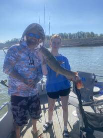 A young angler proudly displaying a large fish alongside an adult on a fishing boat, enjoying a sunny day on the water.