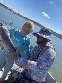 A young angler and an adult proudly displaying a large catfish while fishing on a sunny day.