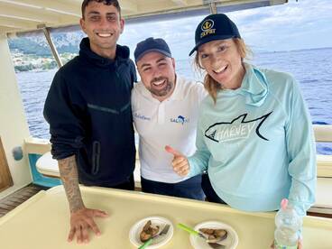 Three individuals enjoying a moment on a boat, with a scenic backdrop of the coastline and ocean.