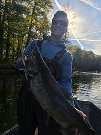 A young angler proudly displaying a large Salmon while fishing on a serene lake surrounded by autumn foliage.