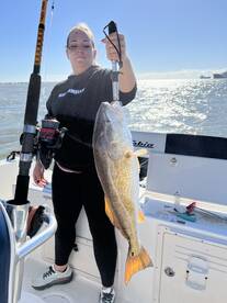 Angler holding a large Redfish while fishing on a sunny day, showcasing a successful catch on the boat.