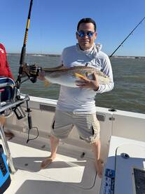 Angler proudly displaying a large Redfish aboard a fishing boat, enjoying a sunny day on the water.