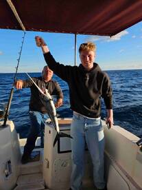 A young angler proudly displaying a fish while fishing on a boat, with a clear blue ocean backdrop.
