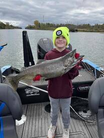 A young angler proudly displaying a large trout while fishing on a calm river, showcasing a successful day on the water.