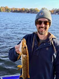 Angler proudly displaying a Northern Pike while fishing on a scenic lake during autumn.