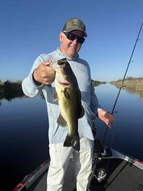 An angler proudly displaying a large Largemouth Bass while fishing on a calm lake, showcasing a perfect day for bass fishing.