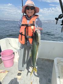 An excited angler proudly displaying a large Yellowtail while fishing on a boat, showcasing a beautiful day on the water.
