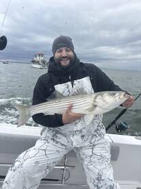 Angler proudly displaying a large Striped Bass while fishing on a boat in overcast conditions.