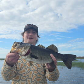 Angler displaying a large Largemouth Bass while fishing in a scenic freshwater environment.