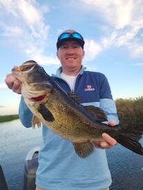 Angler proudly displaying a large Largemouth Bass while fishing in a serene lake setting.