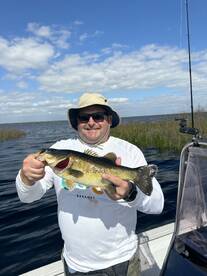 An angler proudly displaying a large Largemouth Bass while fishing on a sunny day in a scenic waterway.
