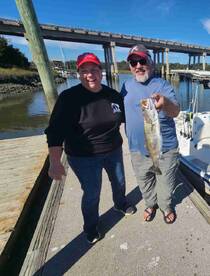 Two anglers happily displaying a large Speckled Trout at the dock, enjoying a sunny day on the water.