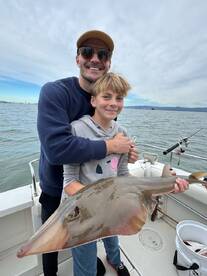 A young angler and an adult proudly displaying a large stingray while fishing on a boat, showcasing a memorable family fishing experience.