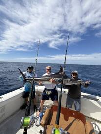 Three anglers proudly displaying a large Mako Shark aboard a sport fishing boat in open waters.
