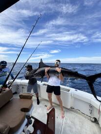 Angler proudly displaying a large Marlin aboard a sport fishing boat in open waters, showcasing a successful deep-sea fishing adventure.