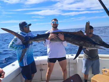 Two anglers proudly displaying a large Sailfish aboard a fishing boat in open waters, showcasing a successful deep-sea fishing trip.