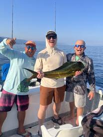 Three anglers celebrating a successful catch of a large Mahi Mahi while fishing in calm waters.