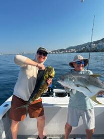 Two anglers proudly displaying their catches, a Mahi Mahi and a Jack Crevalle, while fishing on a sunny day in a coastal area.