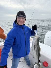 A young angler proudly displaying a large Striped Bass while fishing on a boat, showcasing a successful day on the water.