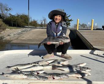 A young angler proudly displaying a large Speckled Trout alongside several other fish on a dock after a successful fishing trip.